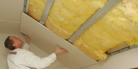 Pracownik montuje płyty gipsowo-kartonowe, kończąc ocieplenie dachu wełną mineralną.