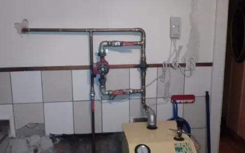 Montaż pompy CO w układzie otwartym. Widoczna instalacja hydrauliczna, czerwona pompa, zawory i fragment kotła.