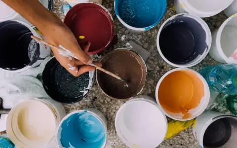 Ręka artysty miesza farby w wiaderkach. Widać różne kolory, ale też potencjalne wady farby ceramicznej, jak nierównomierne rozprowadzenie.