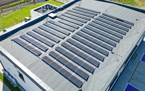Nowoczesny dom z płaskim dachem pokryty panelami słonecznymi, które czerpią energię z promieni słonecznych.