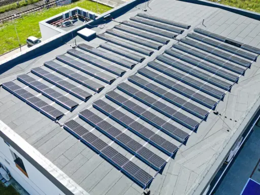 Nowoczesny dom z płaskim dachem pokryty panelami słonecznymi, które czerpią energię z promieni słonecznych.