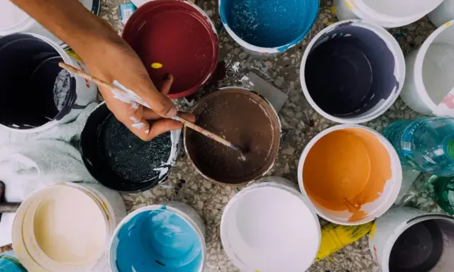 Ręka artysty miesza farby w wiaderkach. Widać różne kolory, ale też potencjalne wady farby ceramicznej, jak nierównomierne rozprowadzenie.