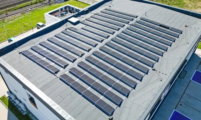 Nowoczesny dom z płaskim dachem pokryty panelami słonecznymi, które czerpią energię z promieni słonecznych.