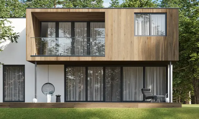 Nowoczesny dom modułowy co to? Elegancka bryła z drewnianą elewacją, tarasem i wiszącym fotelem, otoczona zielenią.